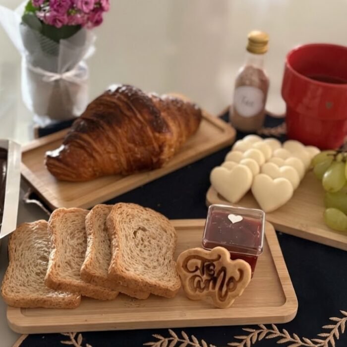 Mesa posta com itens da entrega de cesta de café da manhã em Ibirité: croissant, pães, geleia, bolo, uvas e caneca vermelha